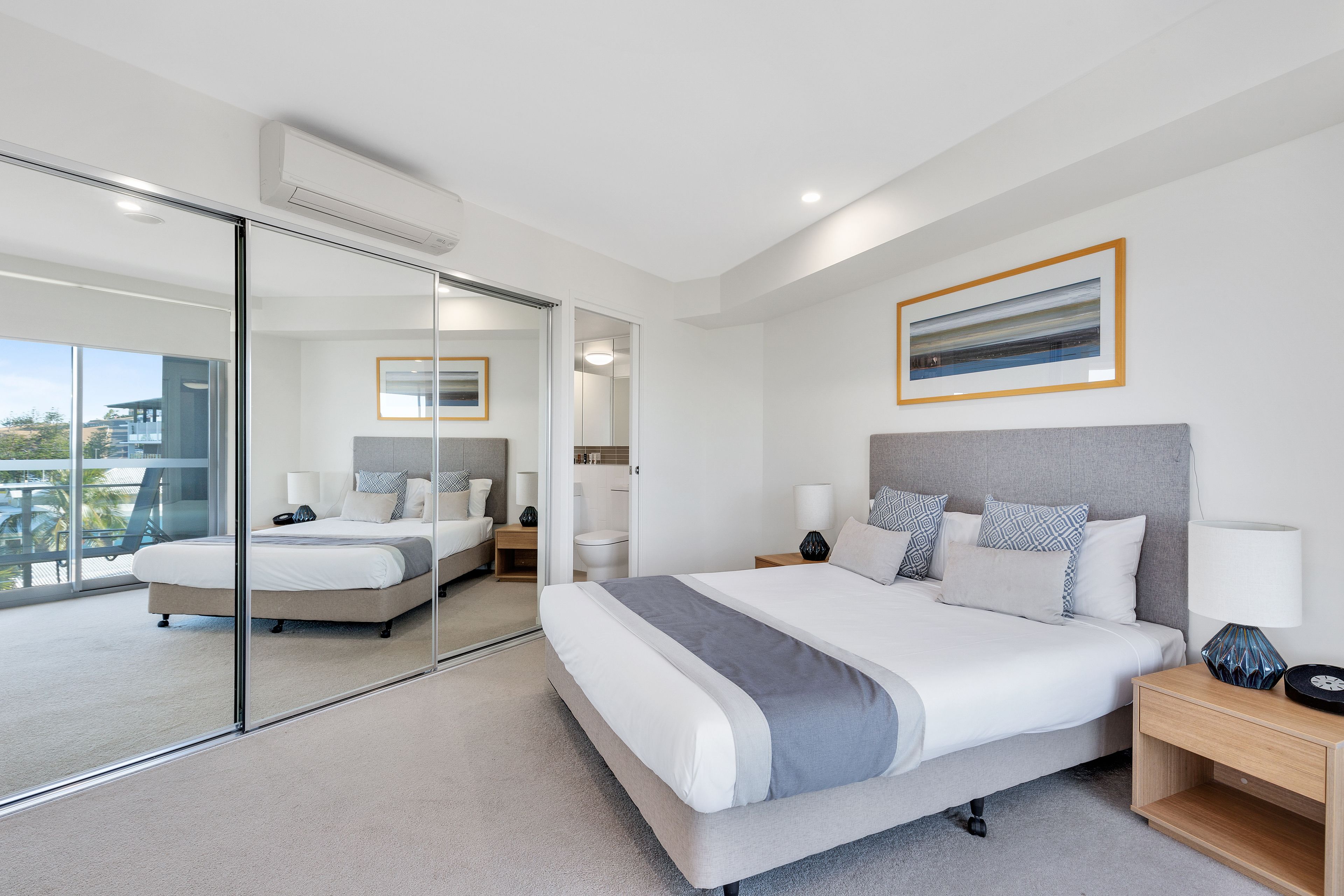 A modern bedroom with a large bed, bedside tables, a mirror, and a view of the outdoors.