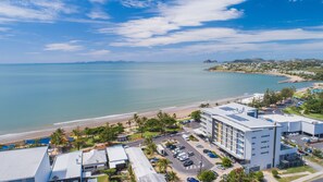 Un hotel costero con vista a la playa, estacionamiento y arquitectura moderna.