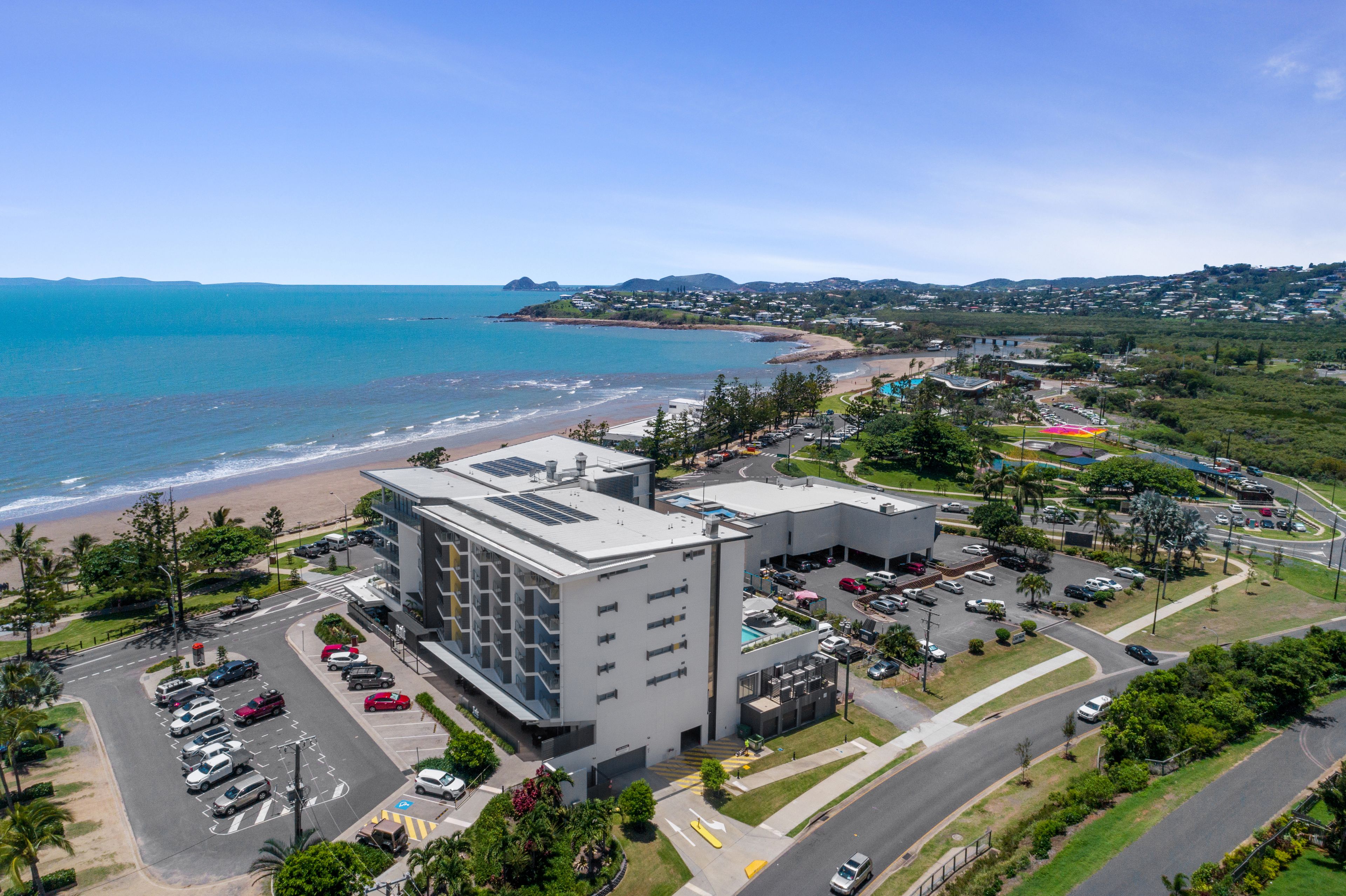 Un hotel costero con estacionamiento, vistas a la playa y una estructura de edificio moderna.