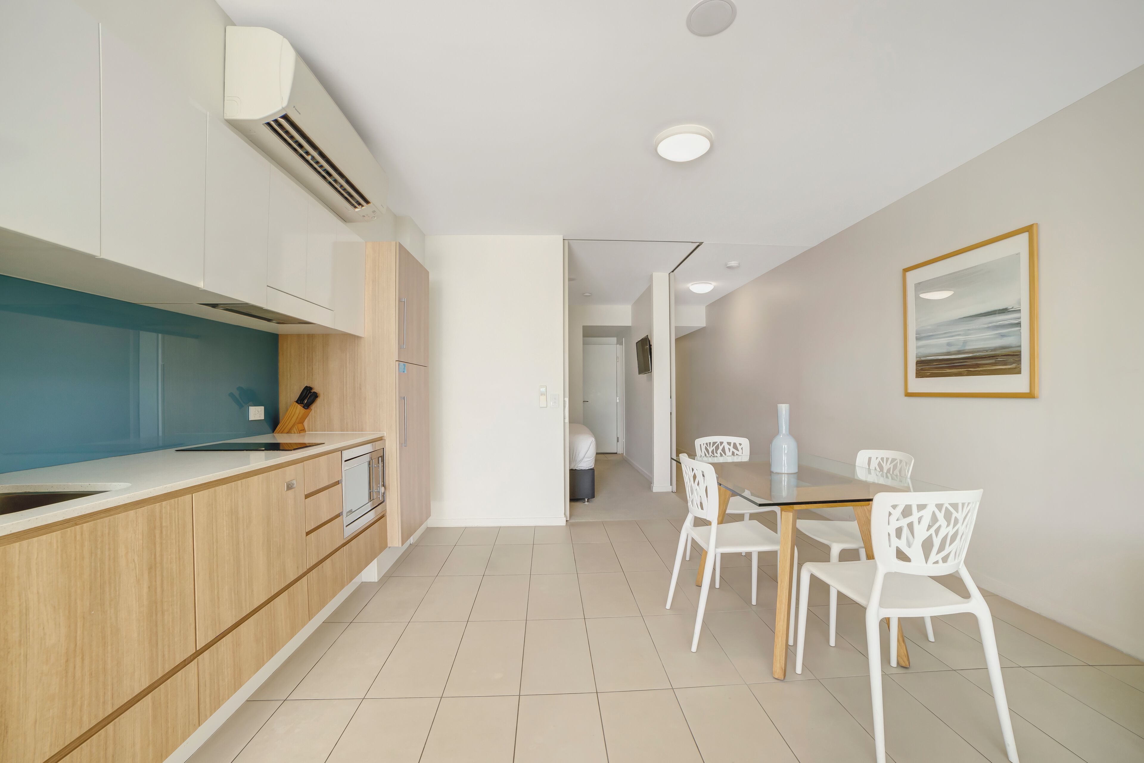 Una cocina moderna con armarios de madera, encimera blanca y un comedor con sillas y mesa blancos.