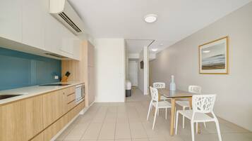 Una cocina moderna con armarios de madera, encimera blanca y un comedor con sillas y mesa blancos.