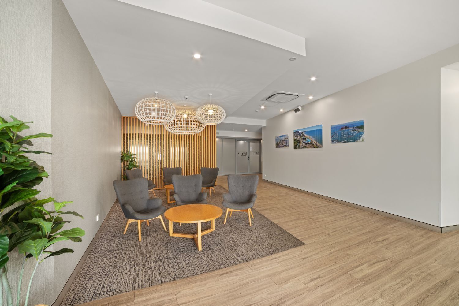 Een moderne kantoorruimte met een vergaderruimte, voorzien van grijze stoelen en een ronde houten tafel, een decoratieve hanglamp en een wand met ingelijste foto’s.