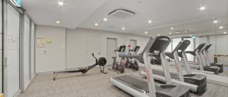 Een fitnessruimte met loopbanden, hometrainers en een roeimachine.