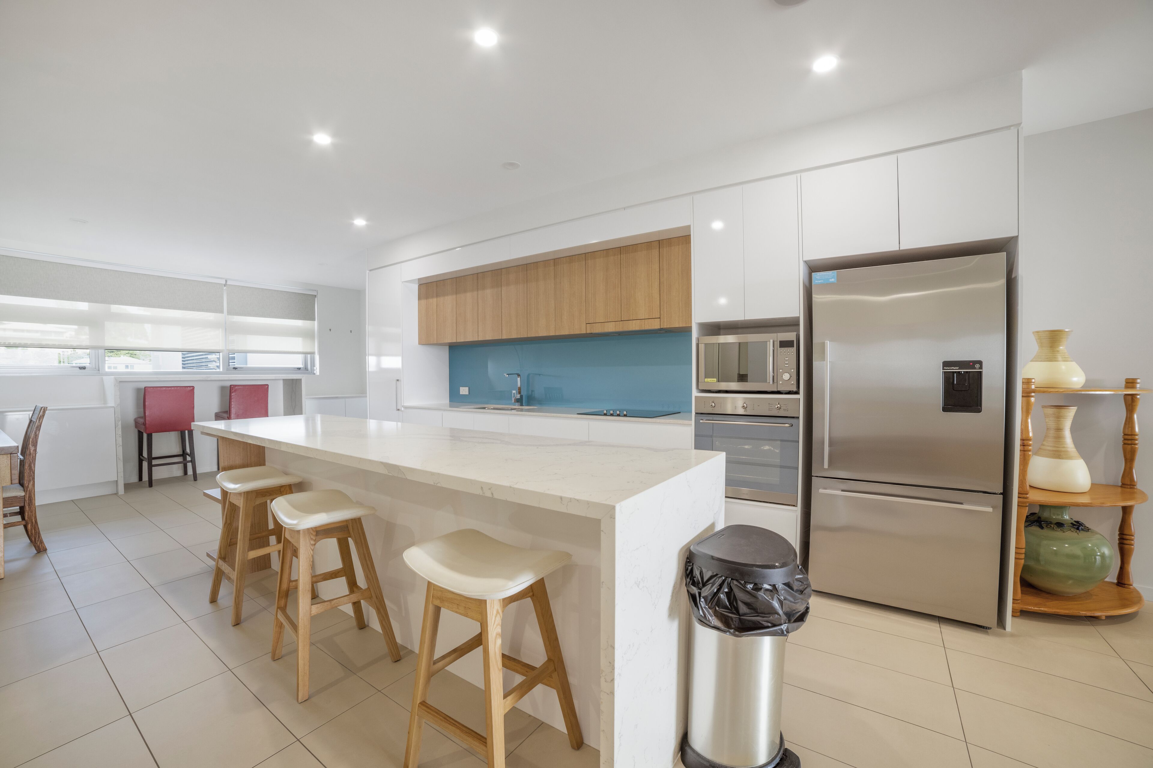 Una cocina moderna con una isla central, taburetes de madera, electrodomésticos de acero inoxidable y vistas al exterior.