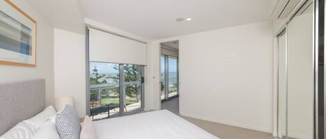A modern bedroom with a large bed, a balcony with a glass door, and a view of the outdoors.
