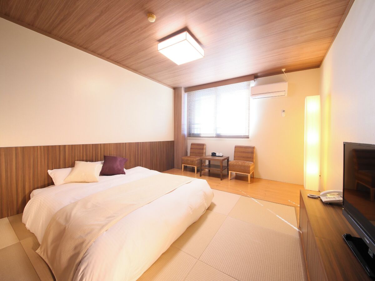 A hotel room with a bed, a TV, a desk, and a chair.