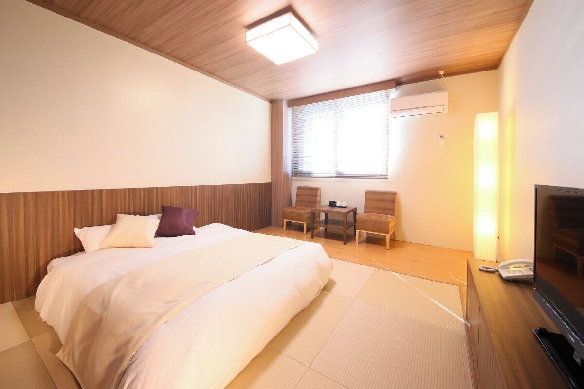 A hotel room with a bed, a TV, a desk, and a chair.