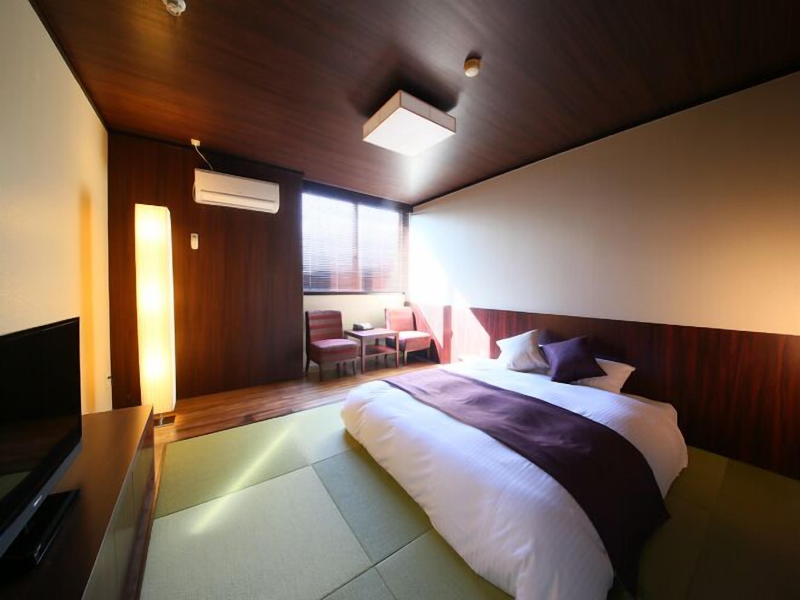 A hotel room with a bed, a desk, a chair, and a TV.
