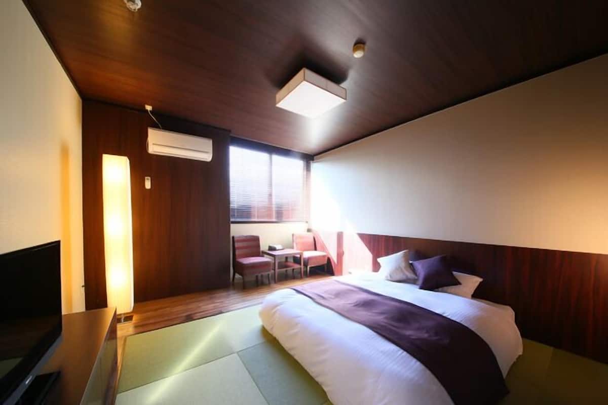 Quarto de hotel com cama, escrivaninha, cadeira e televisão.