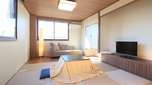 A modern, minimalist living room with tatami flooring, a sofa, a television, and a large window providing natural light. - Nasu Ichiya Hotel (Nasu)