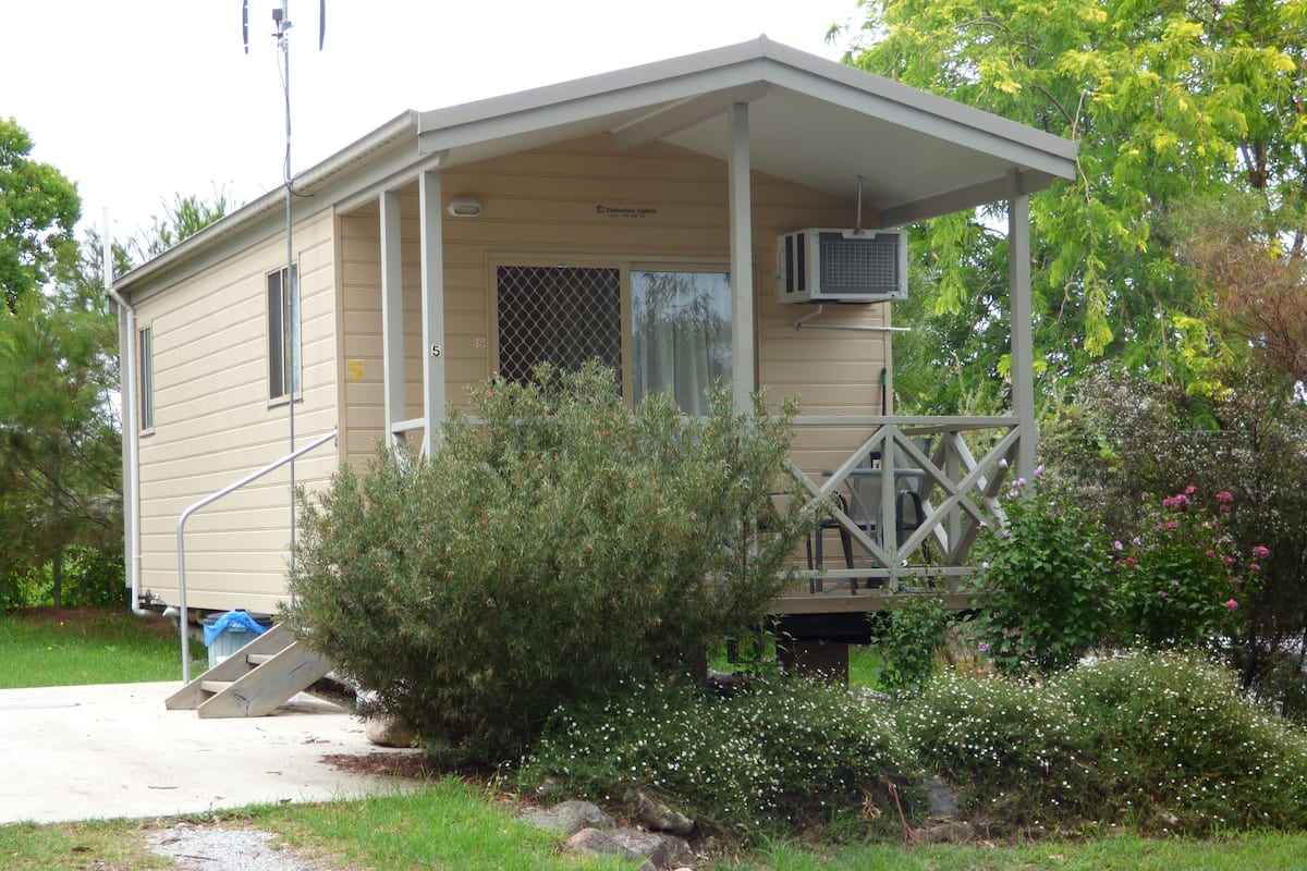 A small, single-story cabin with a porch, a covered outdoor seating area, and a small staircase leading to the entrance.