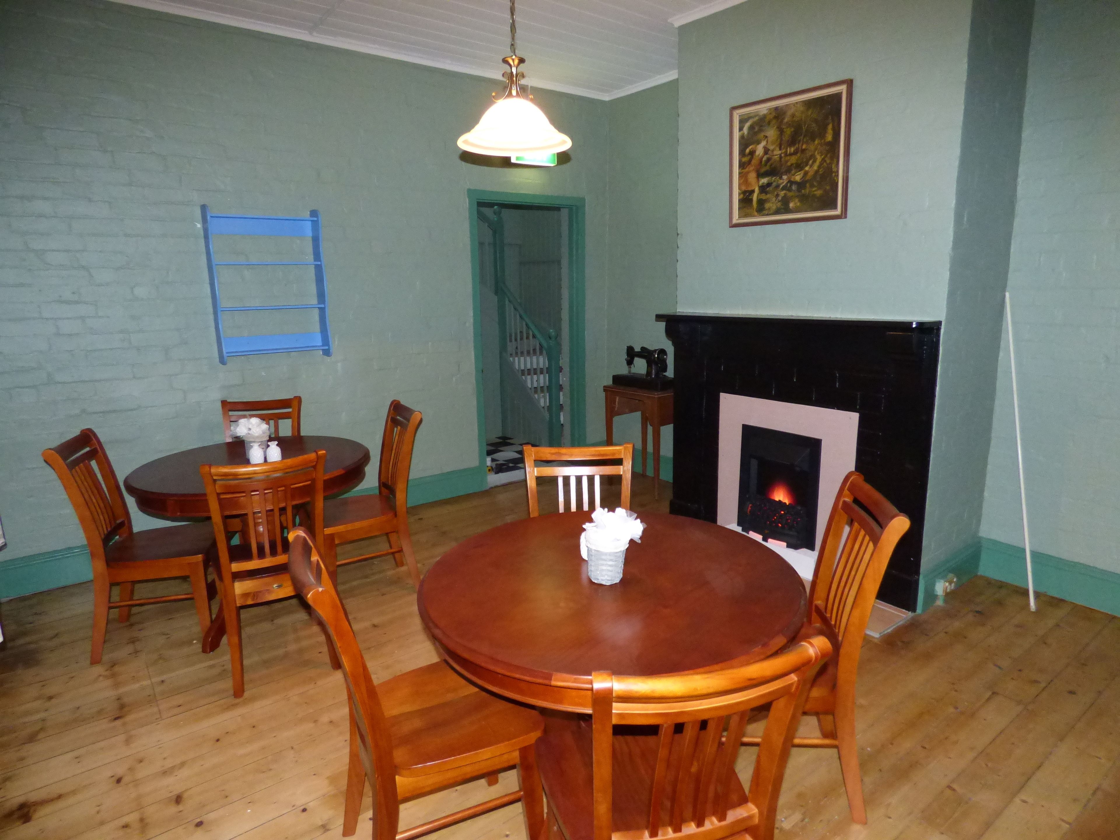 A dining room with a round wooden table and chairs, a hanging light fixture, a fireplace, and a staircase leading to another room.