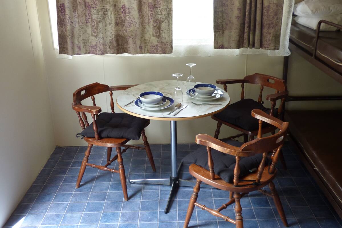 A small dining area with a round table, four wooden chairs, and a bunk bed in the background.
