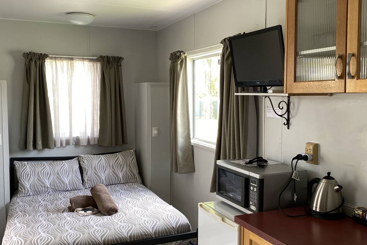 A compact room with a bed, kitchenette, and a television.