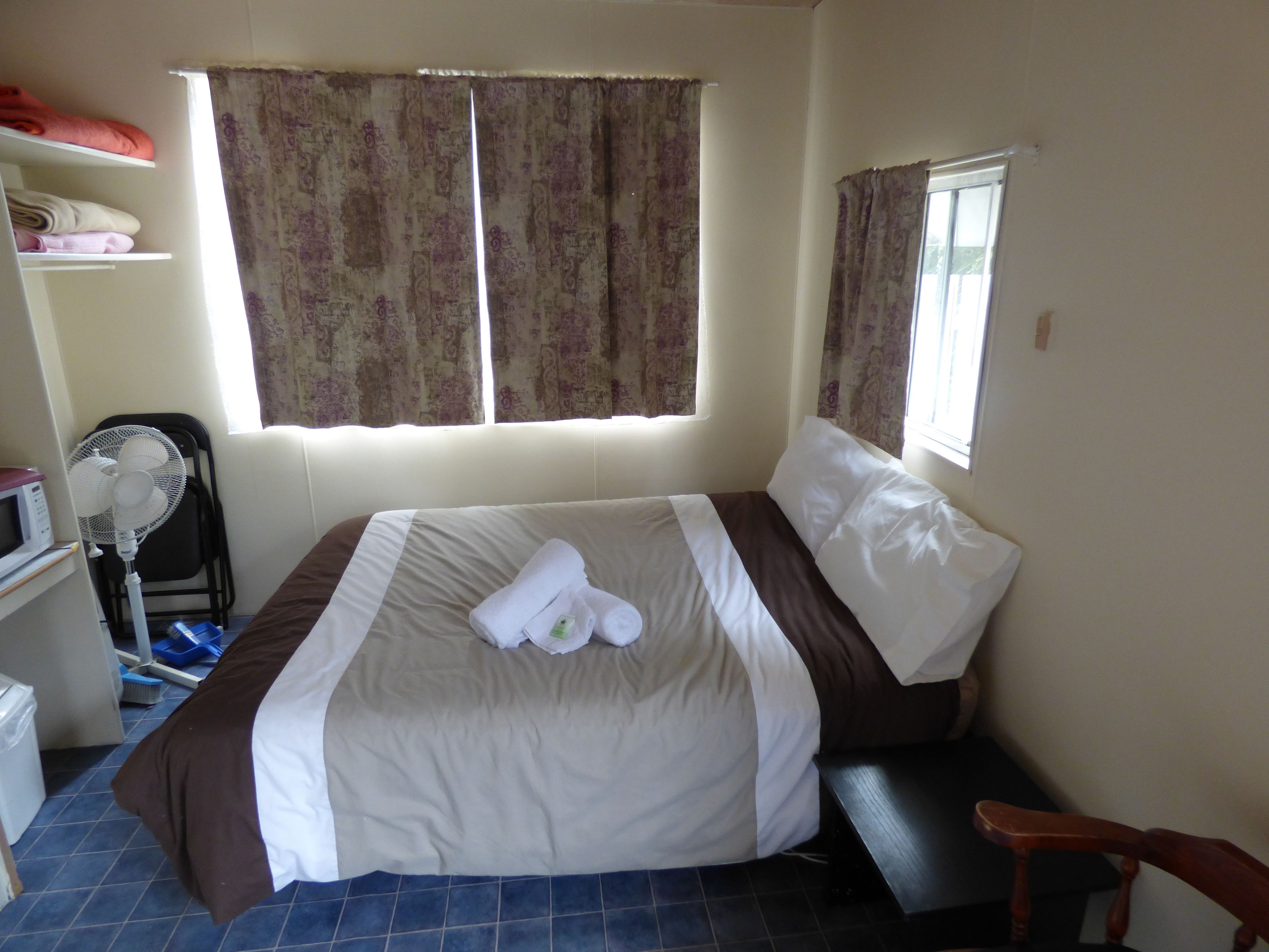 Una habitación de hotel con una cama, un ventilador, un escritorio y una ventana con cortinas.