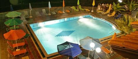 A swimming pool with lounge chairs and umbrellas, surrounded by a tiled deck.