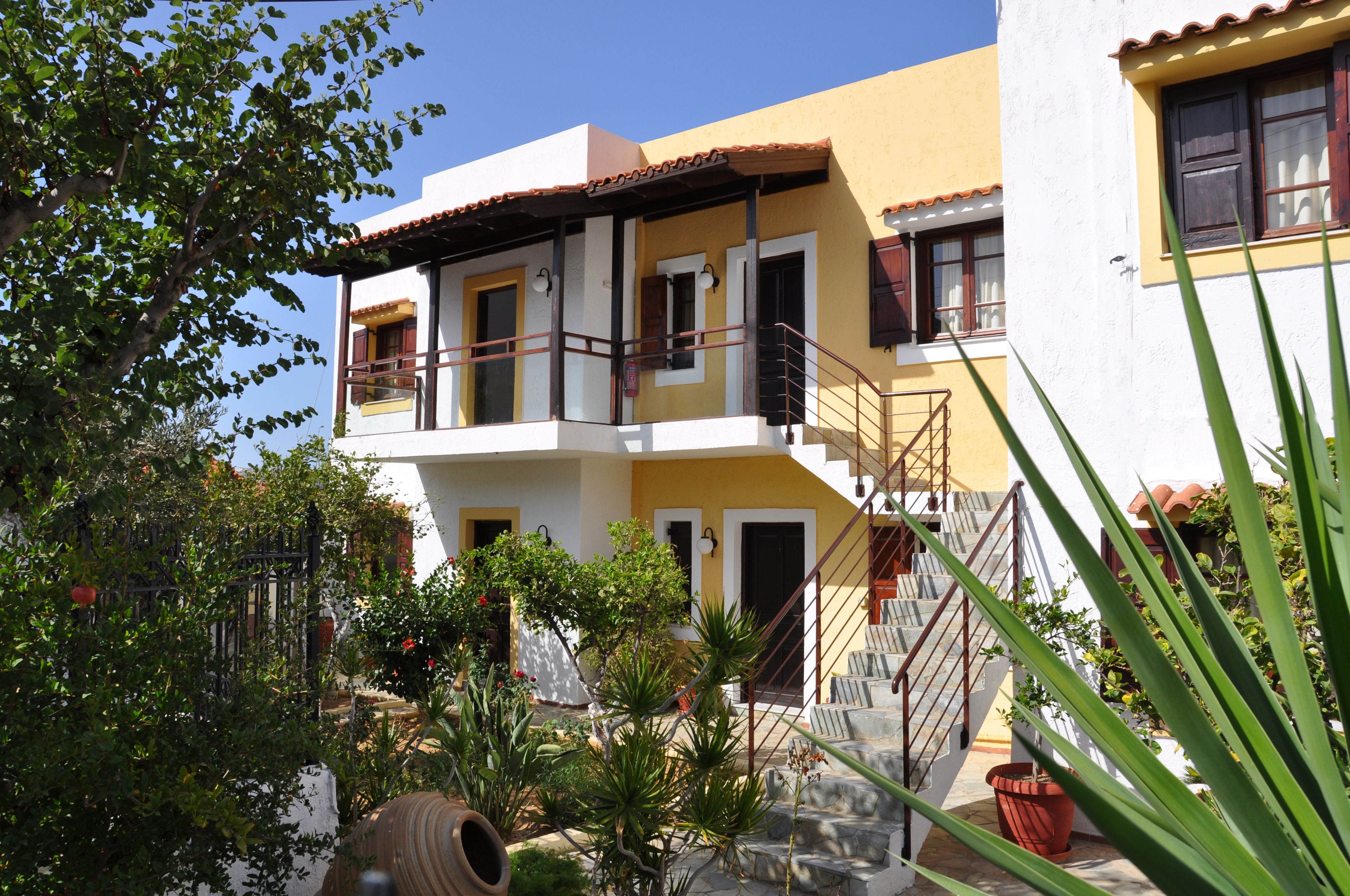 A two-story building with a balcony, a staircase, and a garden with potted plants.