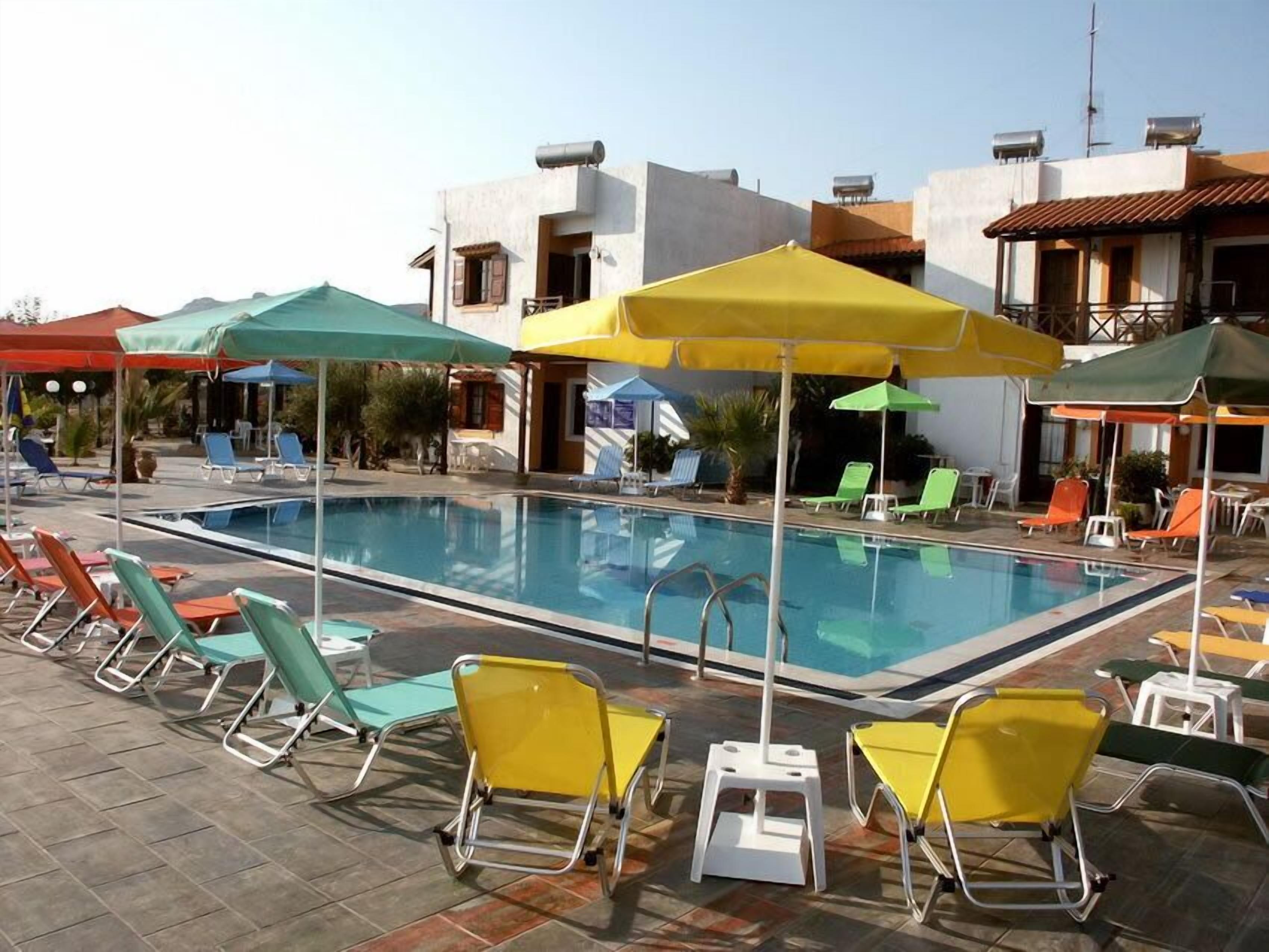 A swimming pool with sun loungers and umbrellas, surrounded by buildings with balconies and water tanks on the roofs.