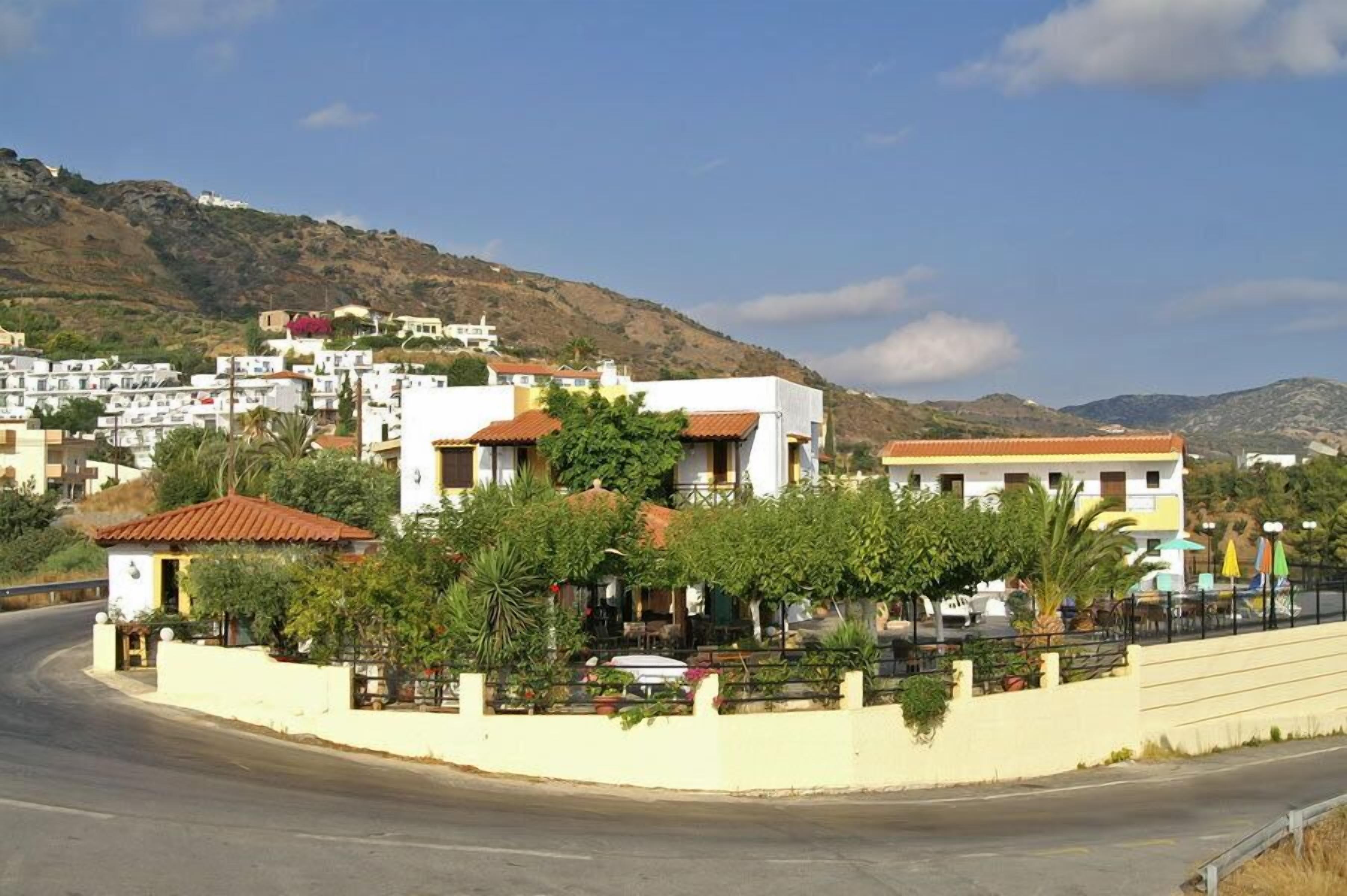 Uma vila costeira com edifícios brancos, uma estrada sinuosa e uma encosta ao fundo.
