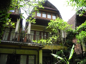 A traditional two-story building with a balcony, surrounded by lush greenery.