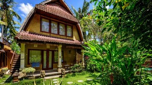 A two-story house with a tiled roof, a porch with a bench, and a garden with tropical plants. - Villa Jineng Ubud Bali (Ubud)