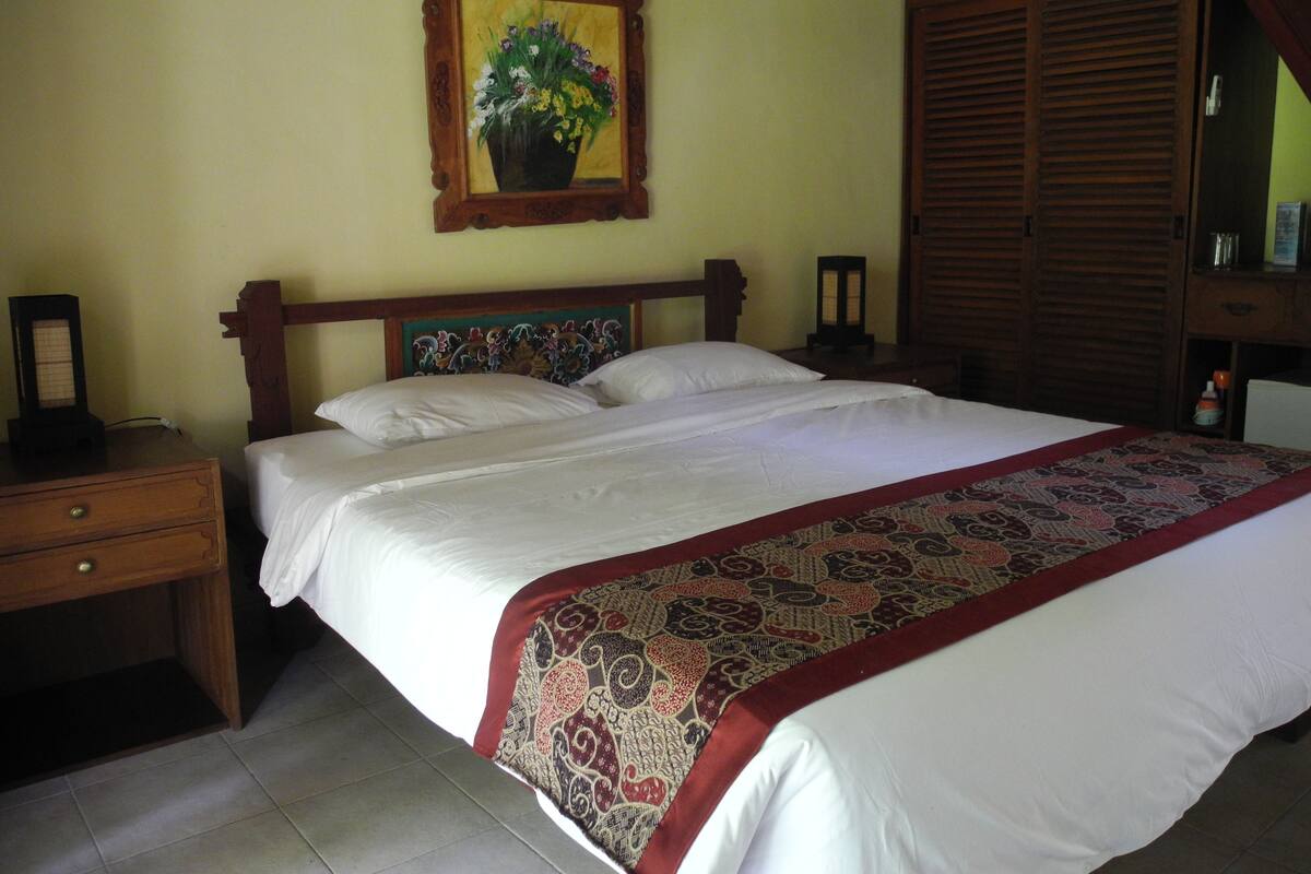A neatly made bed with a patterned bedspread, a wooden headboard, and a nightstand with a lamp.