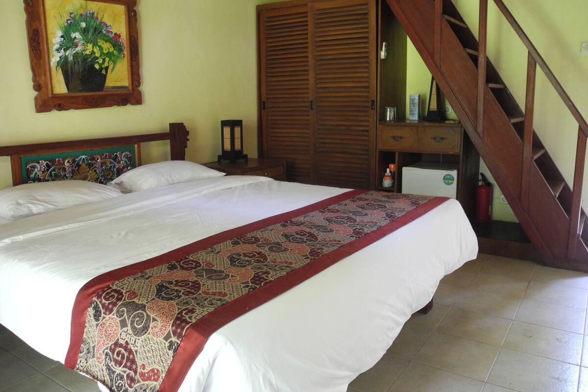 A bedroom with a large bed, a wooden wardrobe, a desk with a chair, and a staircase.