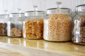 A row of glass jars containing various grains and seeds on a wooden shelf.
