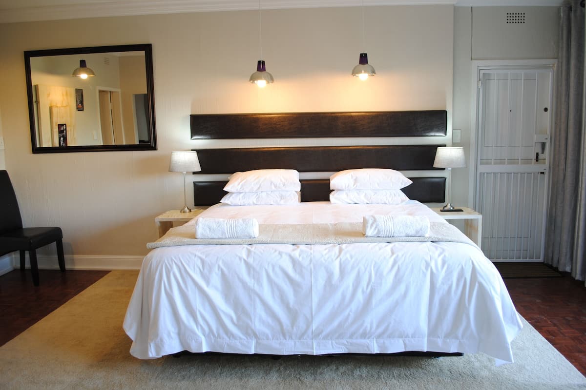 A neatly made bed with white linens, two bedside lamps, a large mirror, and a door with a white frame.