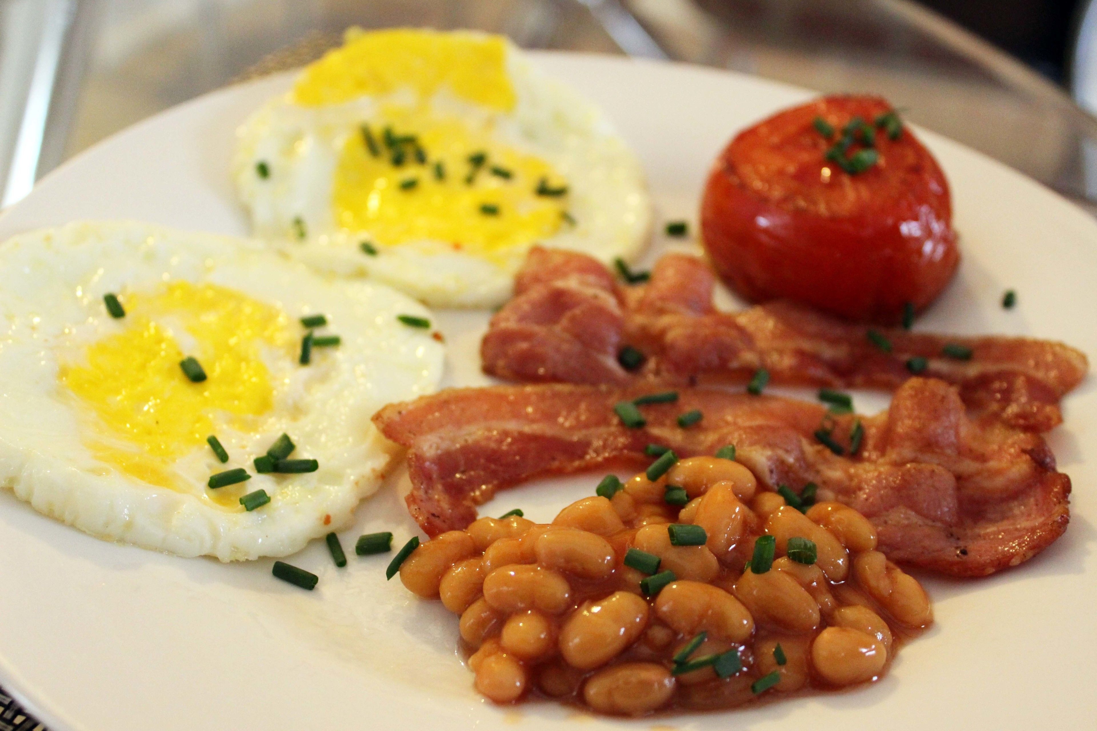 Une assiette avec des œufs, du bacon, des haricots et une tomate.