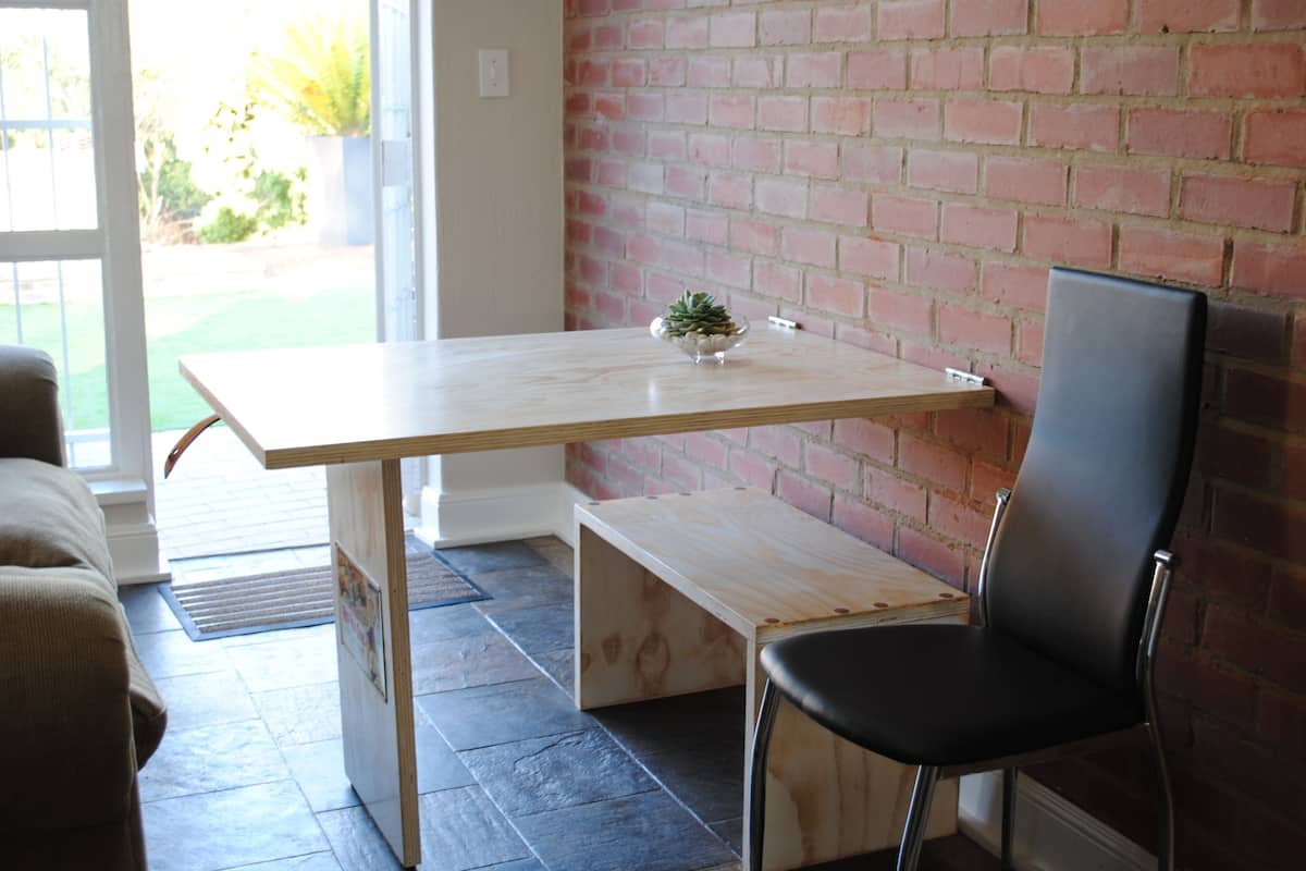 A small, modern room with a wooden table and bench, a black chair, and a brick wall.