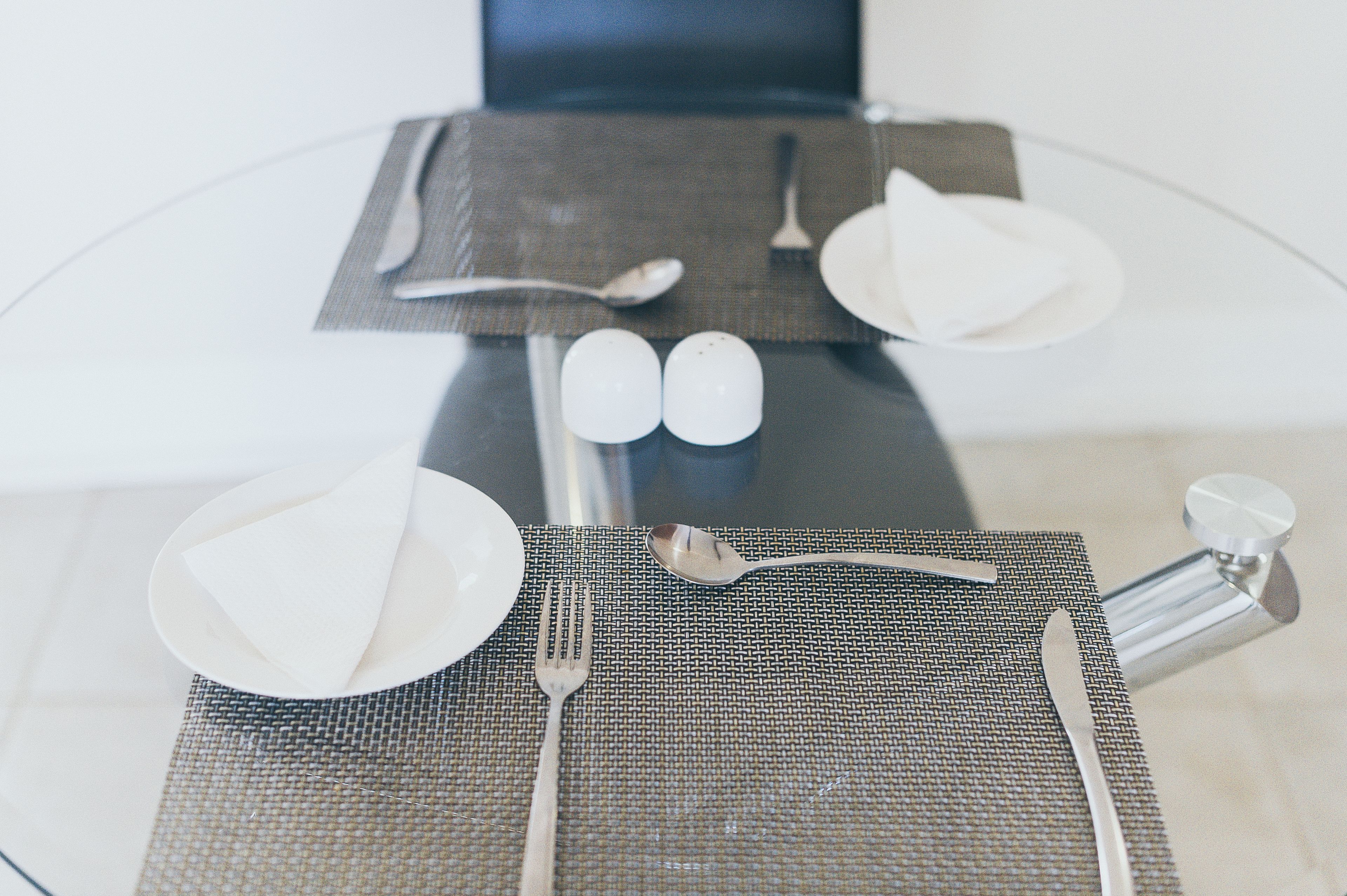 A table set with a placemat, plates, cutlery, and salt and pepper shakers.