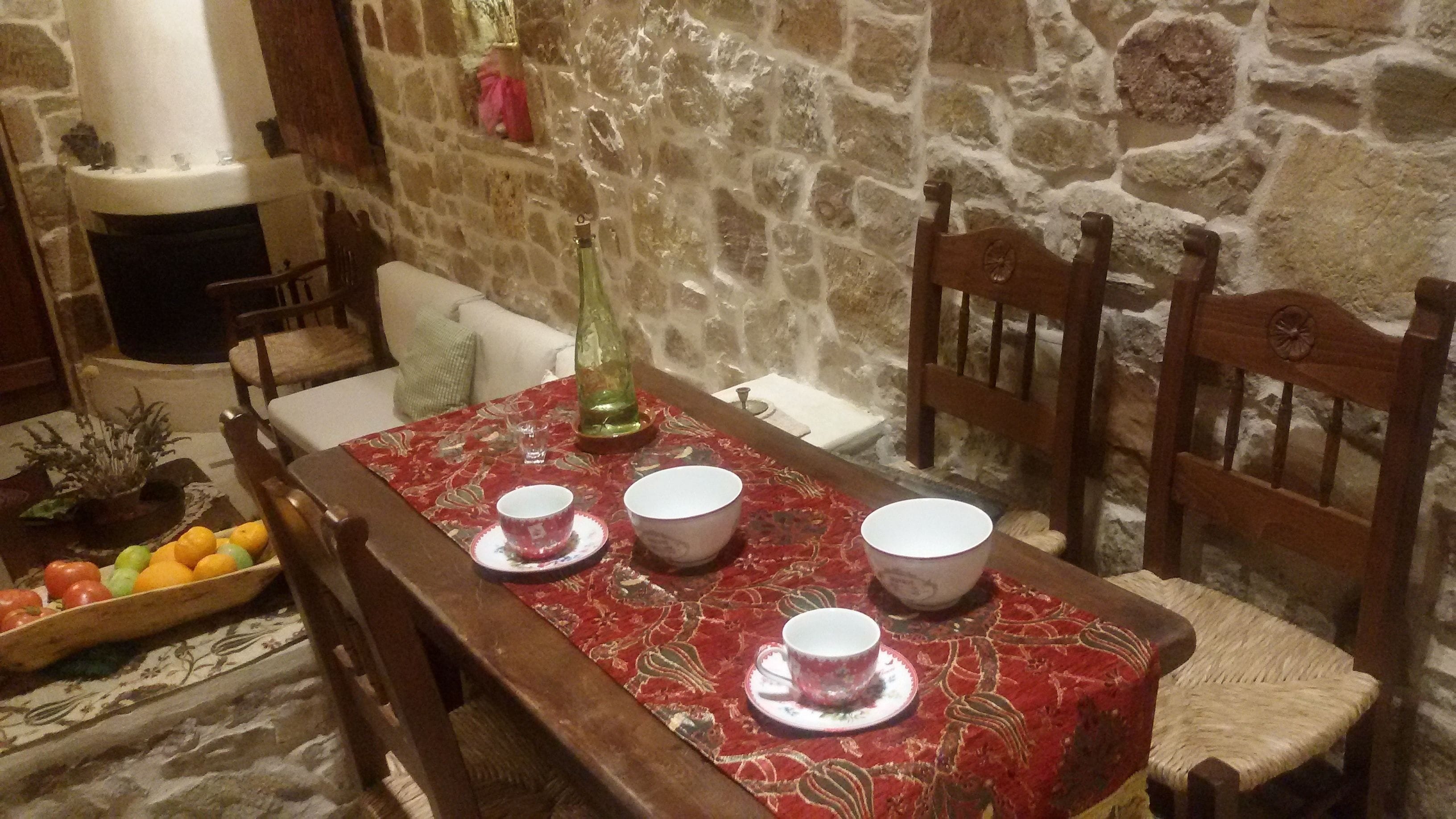 Comedor con pared de piedra, sillas de madera, una mesa con mantel rojo y un frutero.