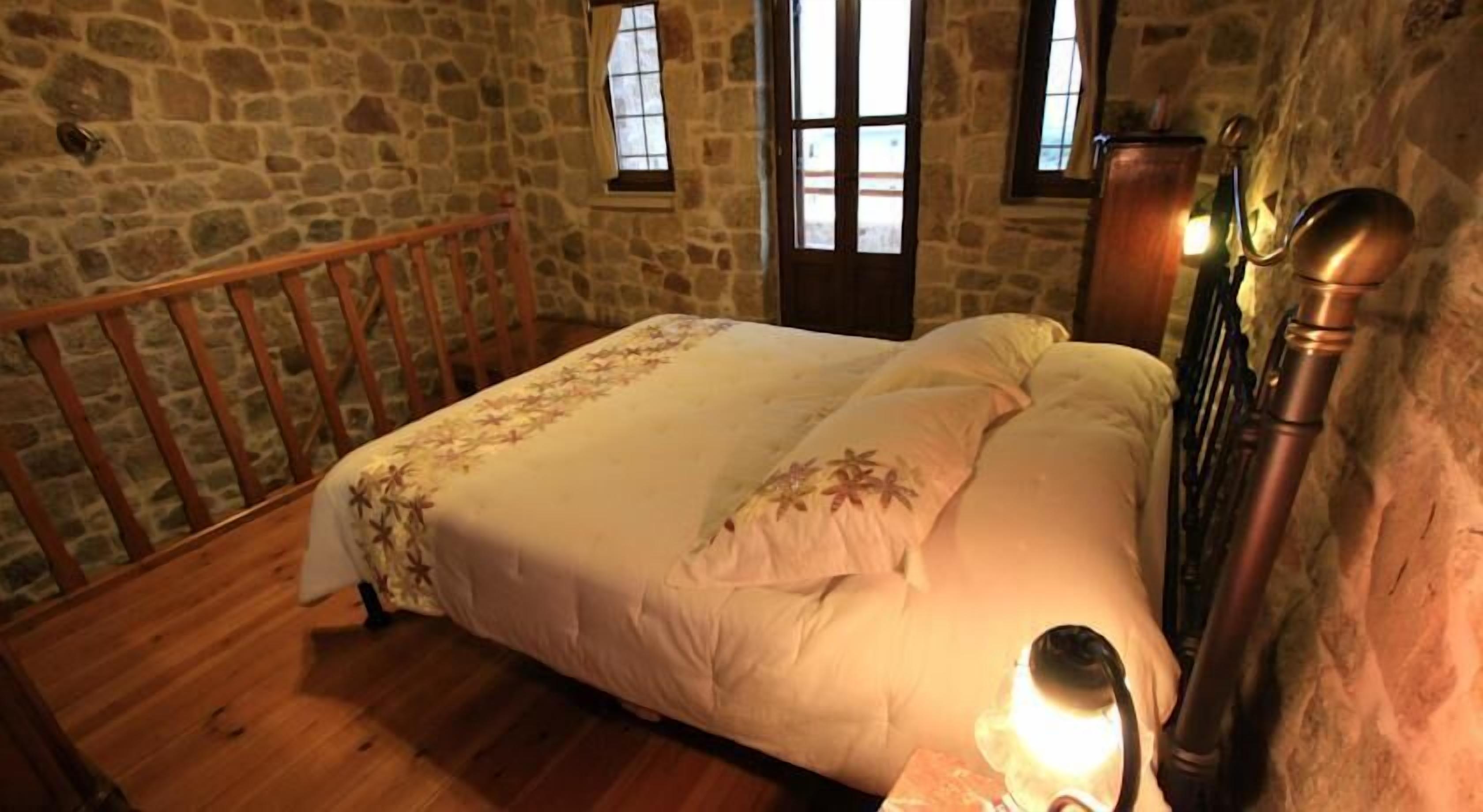 A bedroom with a wooden bed, stone walls, and a wooden railing.