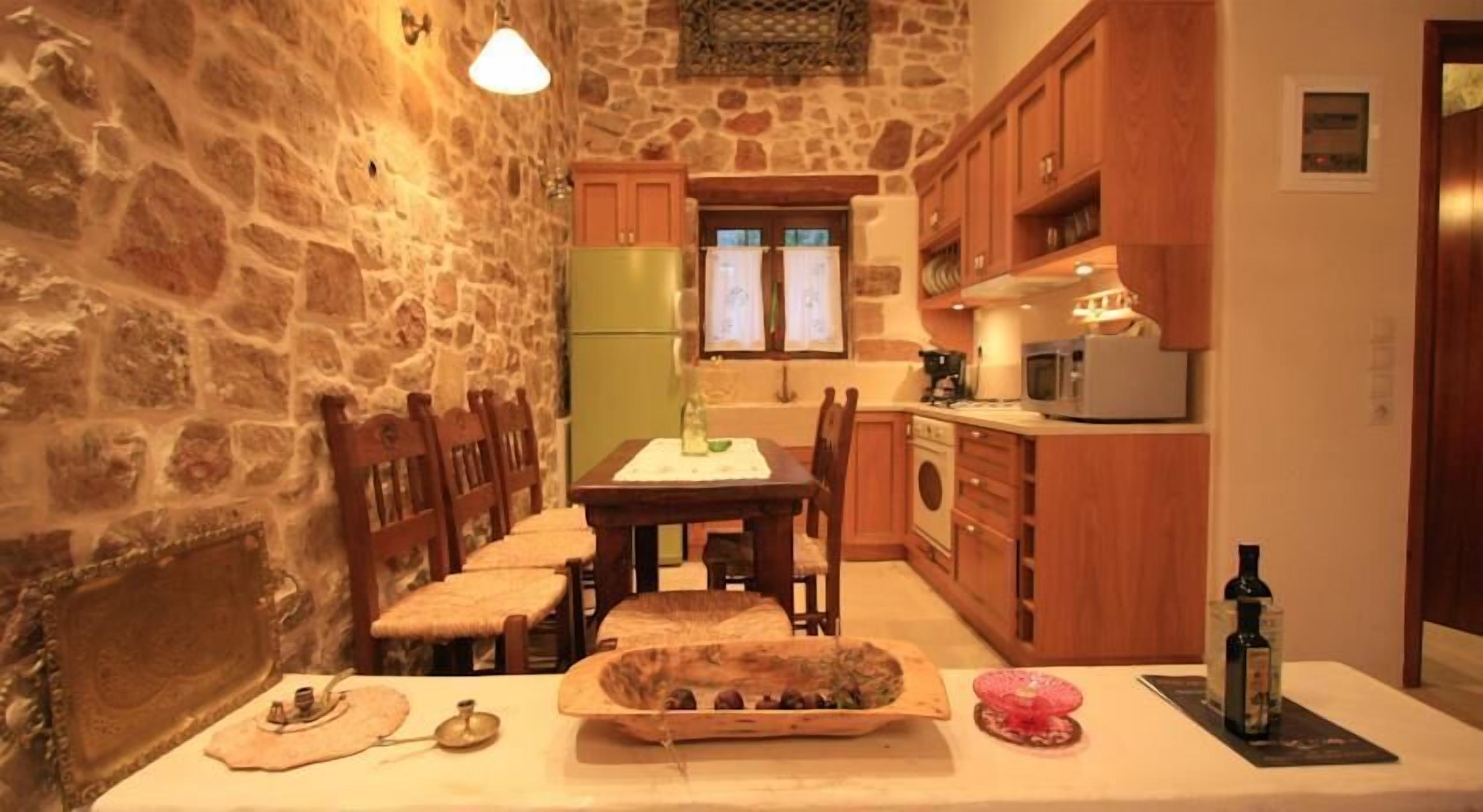 Una cocina acogedora con paredes de piedra, armarios de madera y una mesa de comedor lista para cuatro comensales.