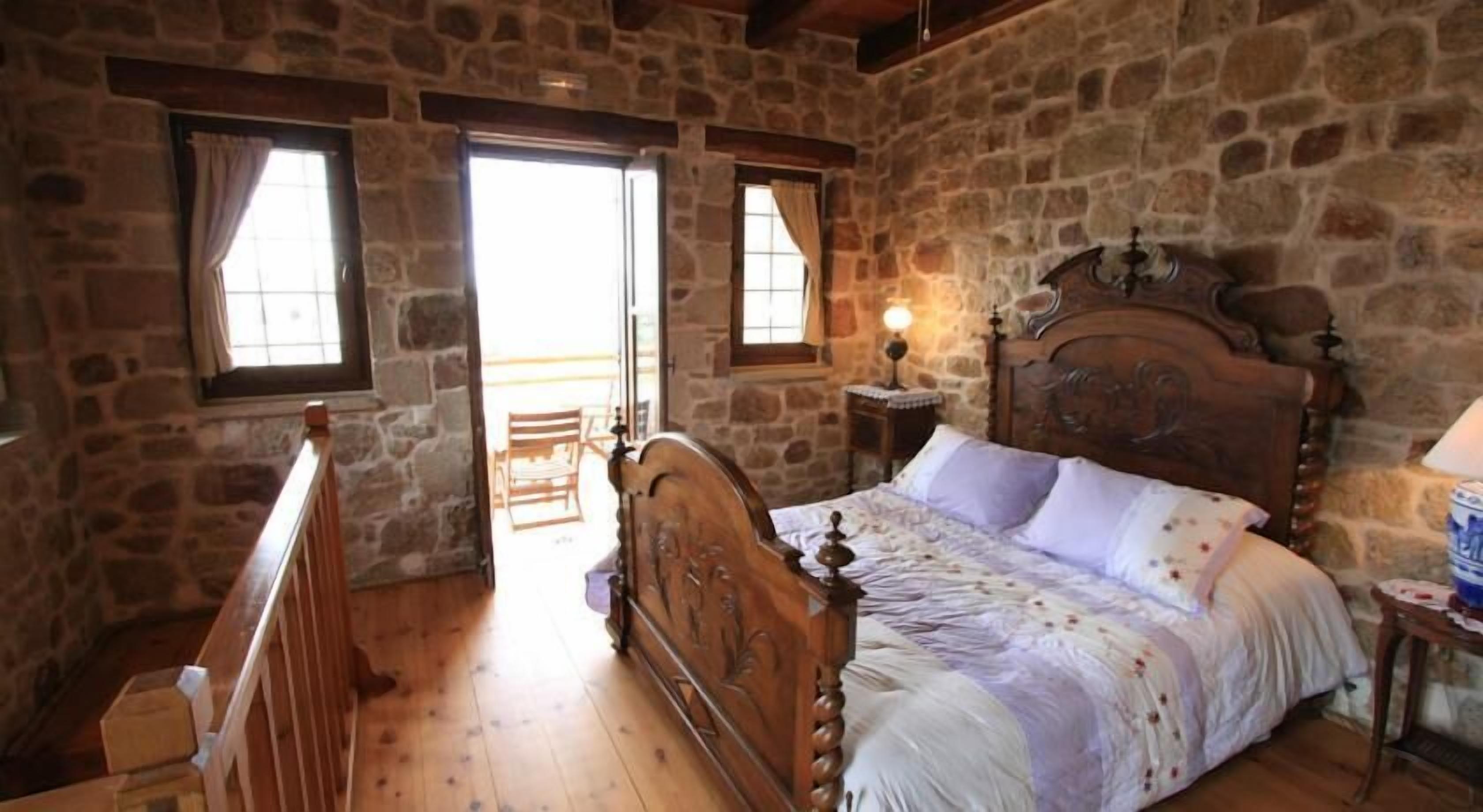 Un dormitorio con cama de madera, paredes de piedra y una ventana.
