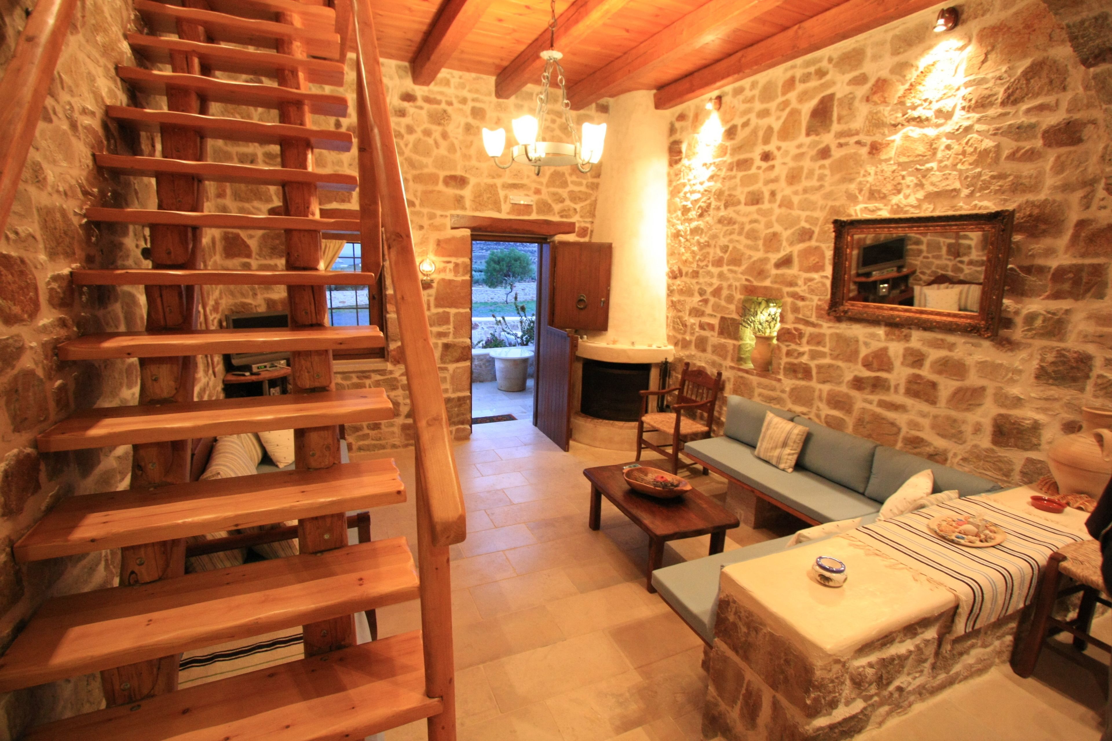 Ein rustikales Interieur mit Steinwand, Holztreppe und einer gemütlichen Sitzecke mit Sofa und Tisch.