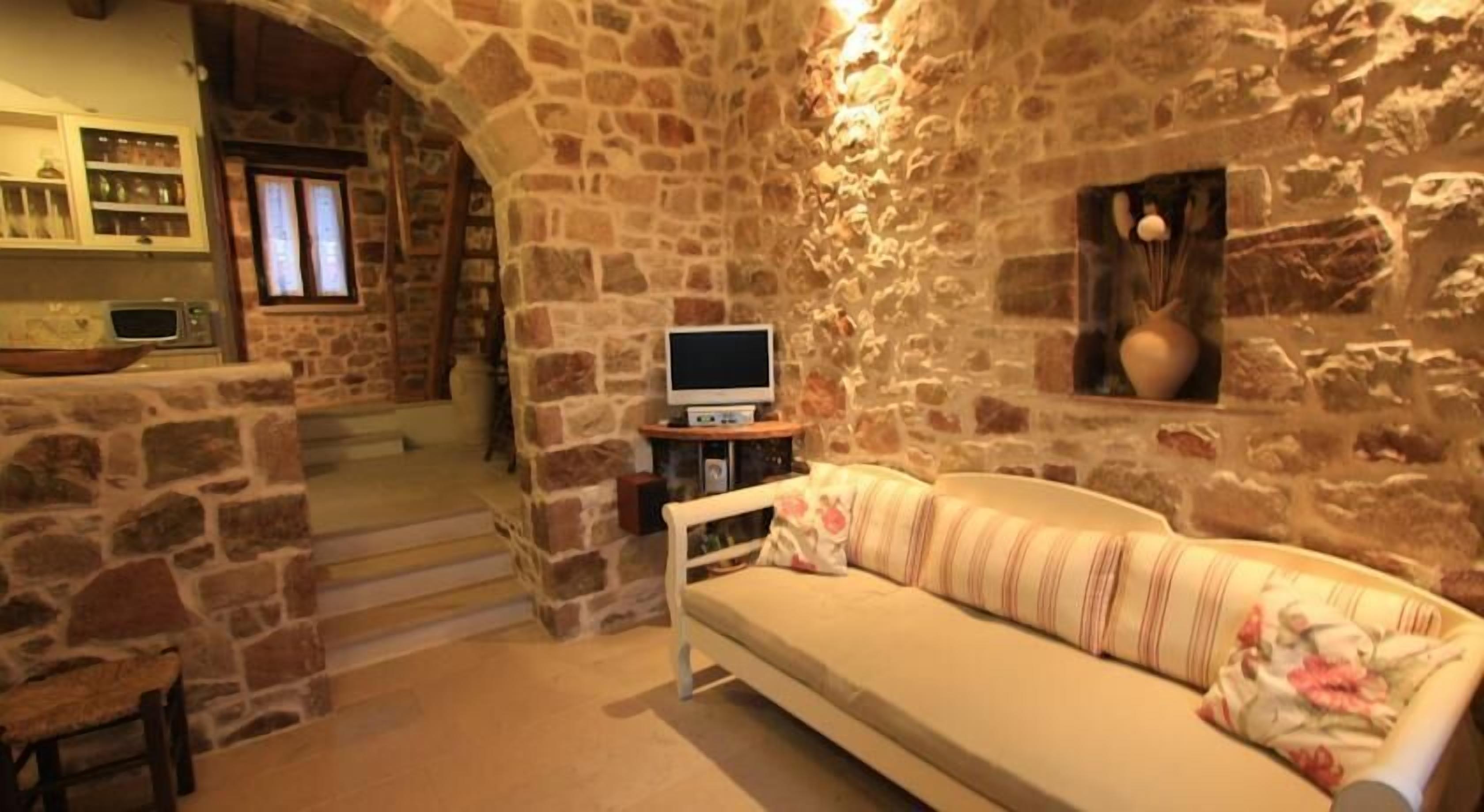 A stone-walled room with a sofa, a television, and a kitchen area with a microwave.