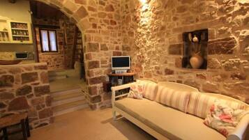 A stone-walled room with a sofa, a television, and a kitchen area with a microwave.