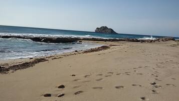 A sandy beach with footprints and seaweed, leading to rocky cliffs and a clear sky.