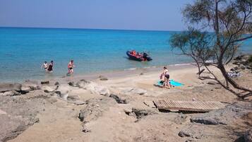 A beach with clear blue water, rocky foreground, and a boat in the distance.