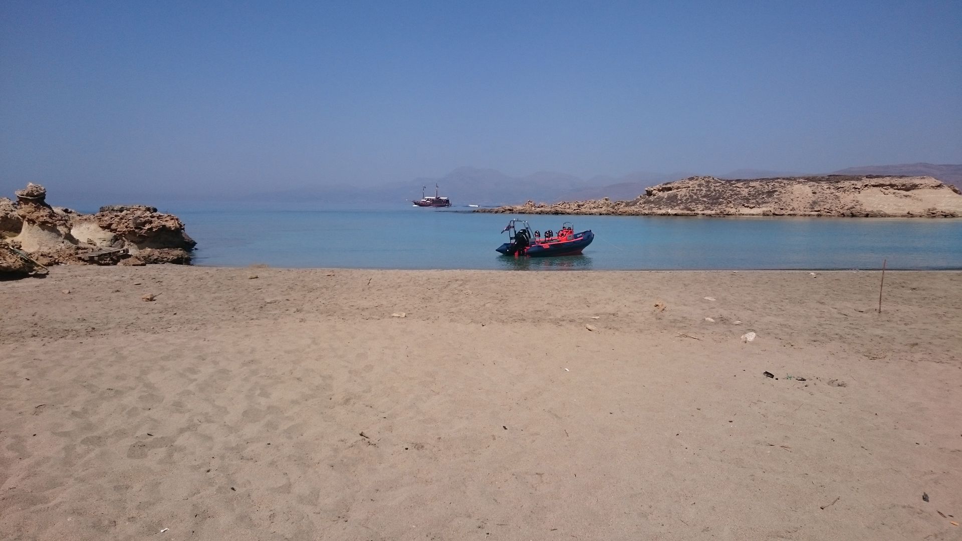 A beach with a boat in the water and a rocky outcrop on the left.