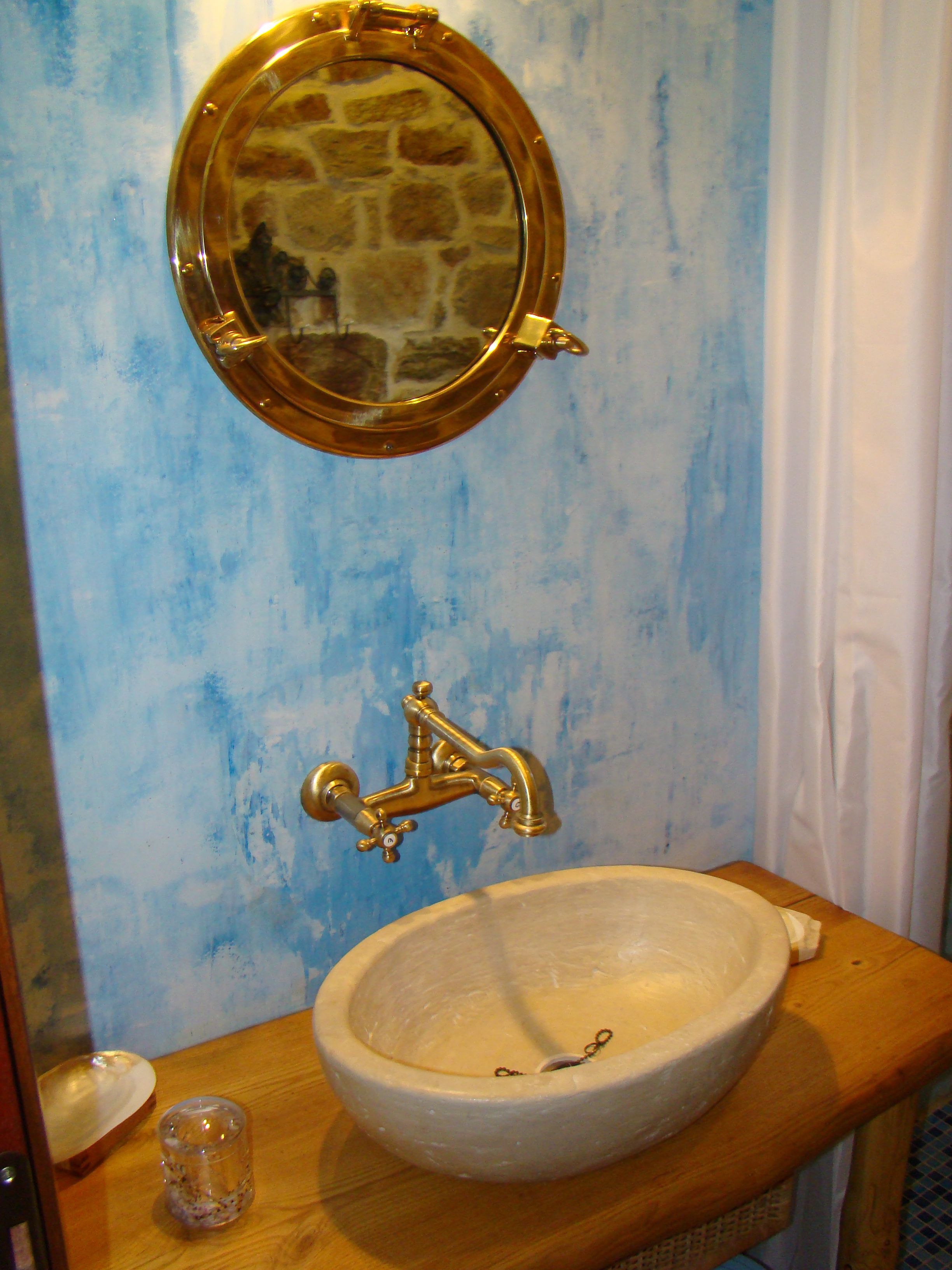 Ein Badezimmer mit einem Steinspiegel, einem Messingarmaturen und einem weißen Waschbecken auf einer Holzplatte.