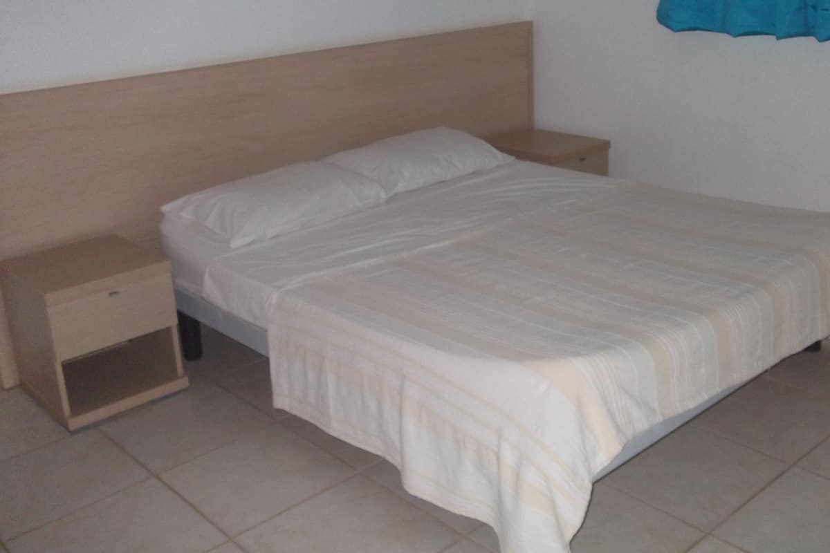 Una cama individual con cabecera de madera, una mesita de noche y un conjunto de cajones.