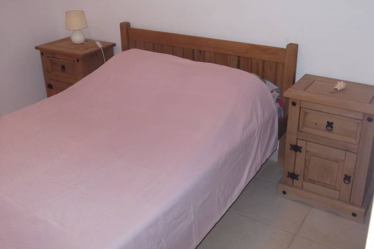 Un dormitorio con una cama de madera, una mesita de noche con lámpara y un pequeño armario de madera.