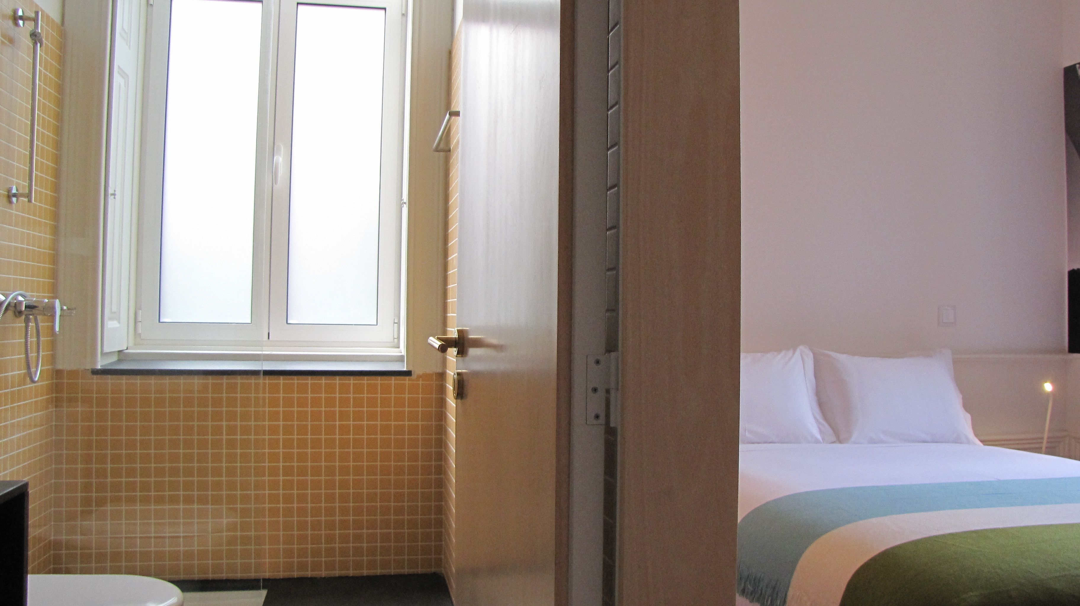 A hotel room with a bathroom, a bed with a striped blanket, and a window with curtains.
