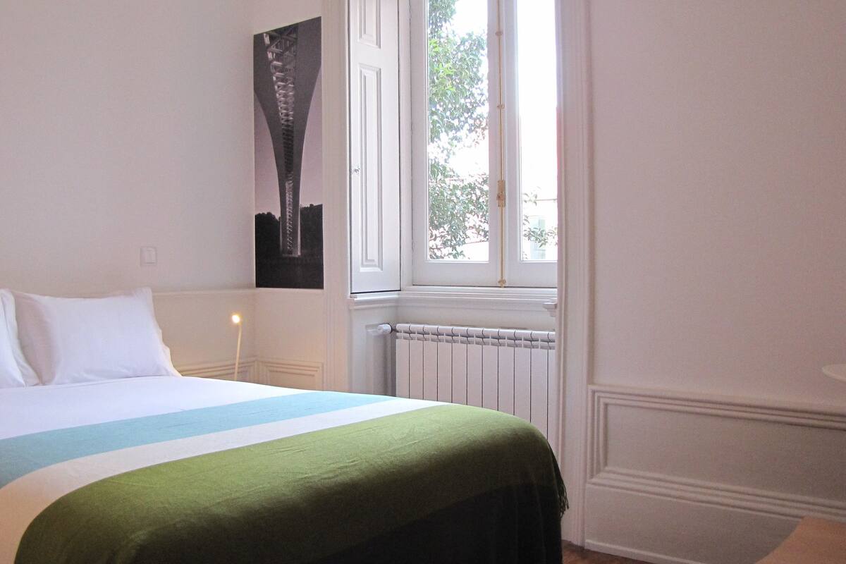 A bedroom with a bed, a window, a radiator, and a wall-mounted picture.