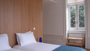 A bedroom with a wooden headboard, a window with a view of greenery, a radiator, and a small wooden stool. - Koolhouse Porto (Porto)