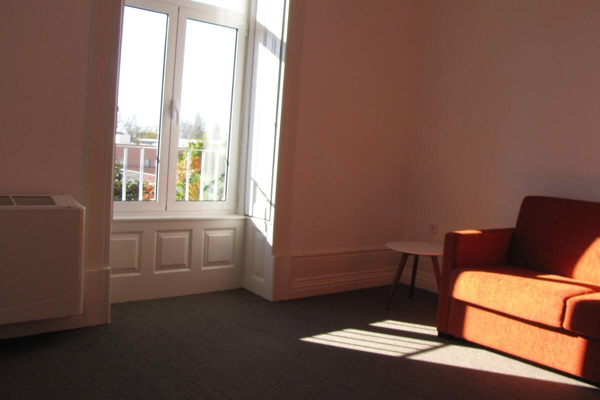 A room with a window, a radiator, a small table, and an orange sofa.