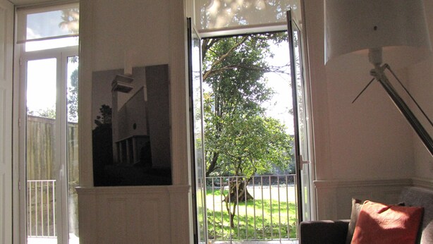 A room with a large glass door leading to a balcony, a framed picture on the wall, and a sofa with a cushion. - Koolhouse Porto (Porto)